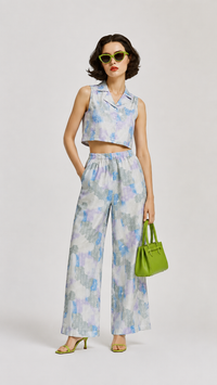 A model wearing the EVERSHE Chromaflora Ocean Lilac floral collared crop-top and wide-leg trouser co-ord set in a light blue, purple, and white watercolor print, showing the front view, styled with lime green sunglasses, a green handbag, and green heels against a light gray studio background.